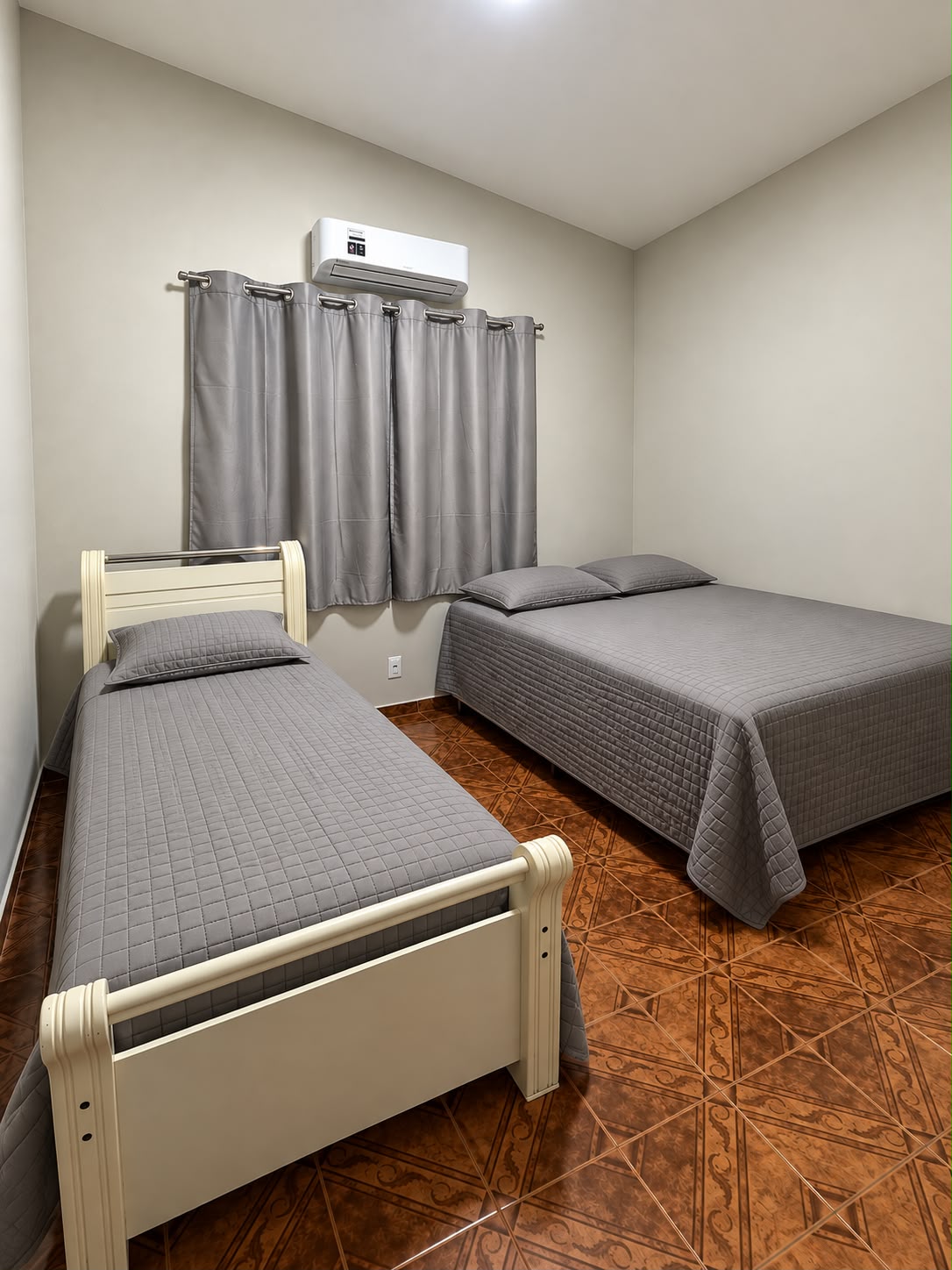 Quarto com cama de solteiro e cama de casal, roupa cinza e parede clara