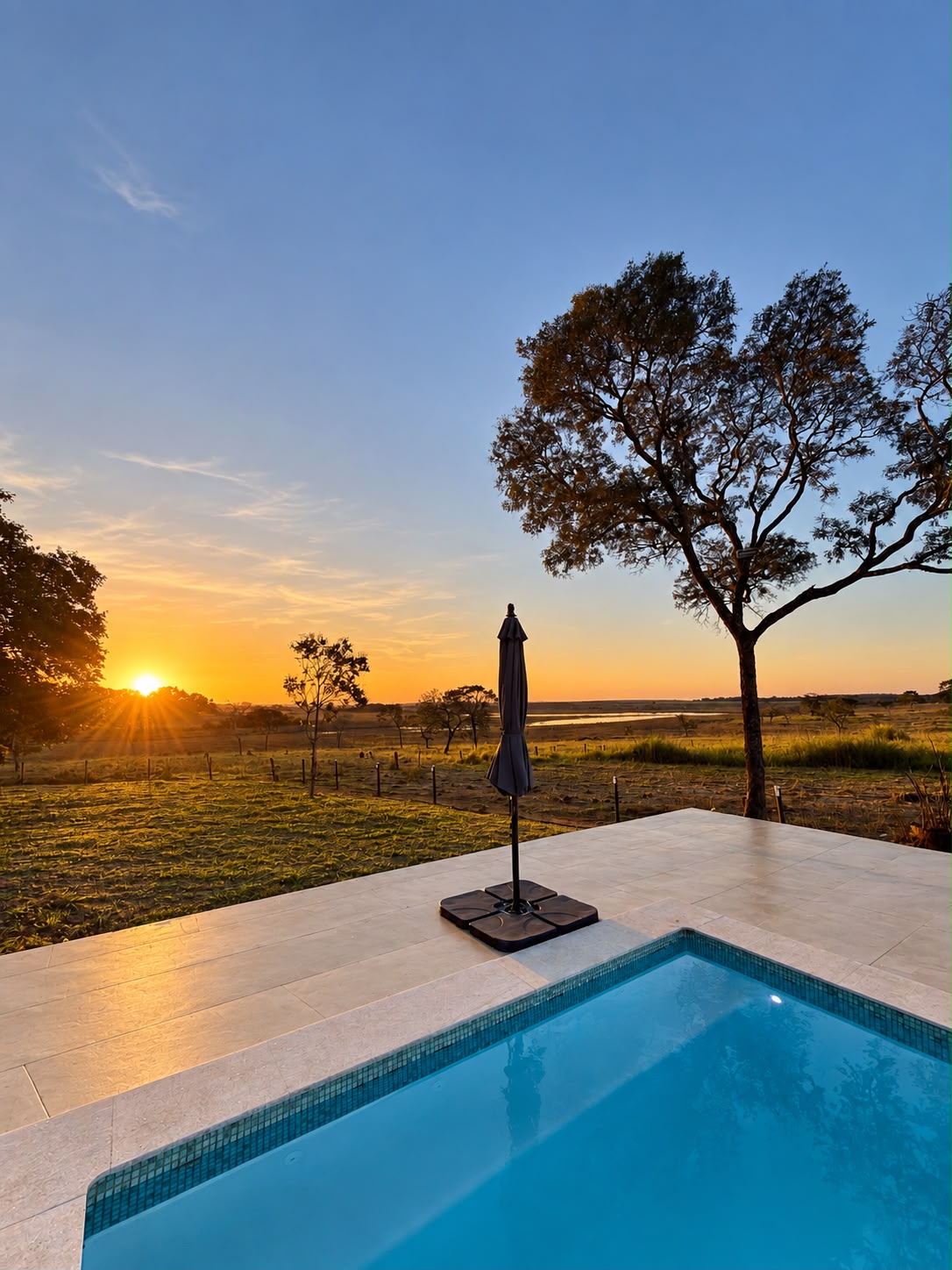 Pátio com piscina e guarda-sol fechado, com vista para o campo ao pôr do sol
